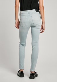 Jeans ajustados de color gris claro con una cintura alta, cuatro bolsillos y un sutil detalle en la parte posterior. Combinados con zapatos negros y una blusa negra.