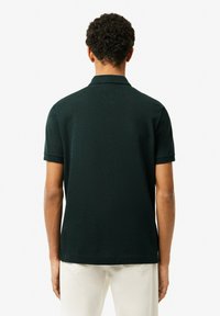 Mörkgrön piké med en strukturerad tyg. Har en klassisk krage, korta ärmar och en rak fåll. Minimalistisk design, inga synliga logotyper.