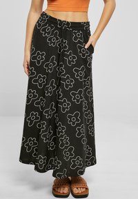 Black maxi skirt with white flower patterns, elastic waistband, and side pockets, worn with brown, woven, flat sandals.