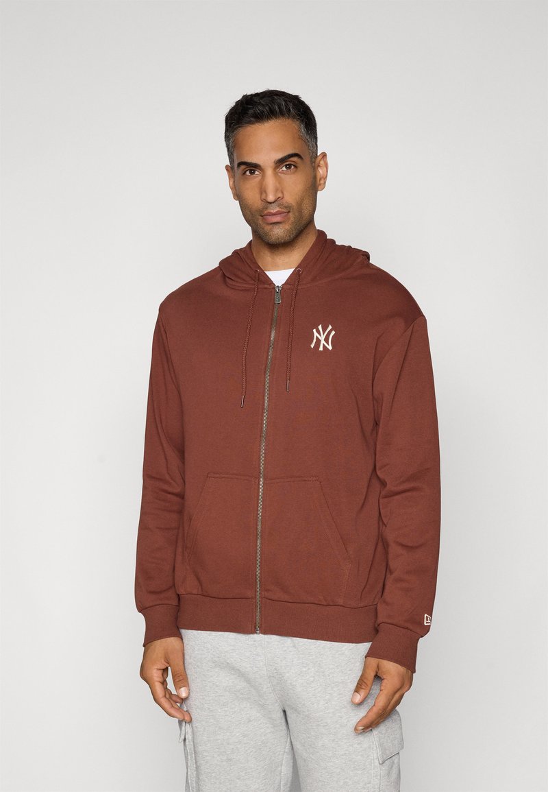 Brązowy hoodie na zamek z kieszenią z przodu oraz białym haftowanym logo na klatce piersiowej. Posiada kaptur ze sznurkiem i ribbowe mankiety.