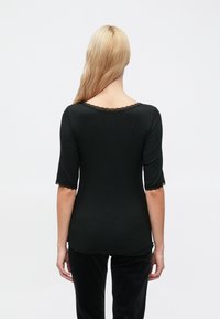 Musta pitkähihainen paita, jossa on aaltoileva pitsikaulus ja kalvosimet, istuva malli ja sileä pinta, yhdistetty tummiin alaosiin.