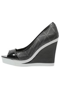 Svart lackläder kilklack med öppen tå, med Calvin Klein-logotyp. Sido vy framhäver den eleganta designen och detaljerna med vit sula.