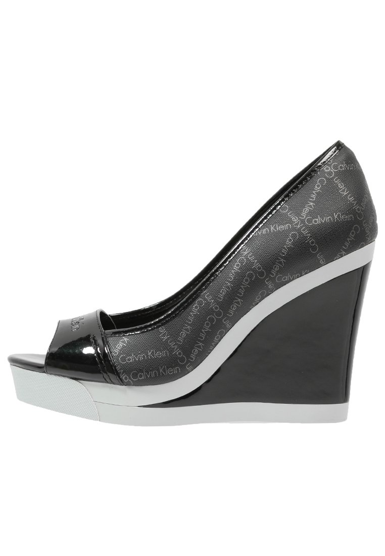 Svart lackläder kilklack med öppen tå, med Calvin Klein-logotyp. Sido vy framhäver den eleganta designen och detaljerna med vit sula.