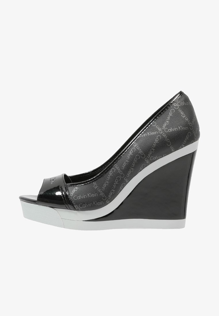 Black patent leather wedge heel with open toe, featuring Calvin Klein branding. Side view highlights sleek design and white sole detail.