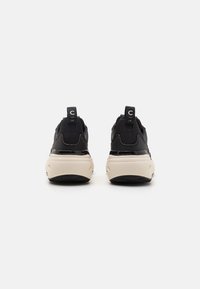 Pair of black sneakers with white chunky soles, viewed from the back, featuring black heel pull tabs with white lettering on a plain background.