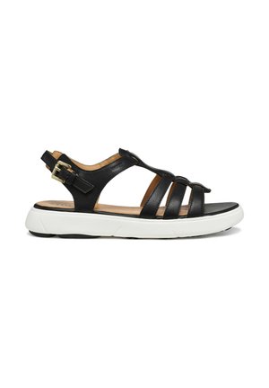 Sandalia de cuero negro con tres tiras delanteras, correa ajustable para el tobillo con hebilla dorada, plantilla acolchada color cuero claro y suela gruesa de goma blanca.