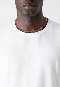 Hvid bomulds t-shirt med rund halsudskæring, der har en glat overflade, parret med et halskæde i guldfarvede led.