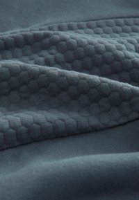 Gestructureerde donkerblauwe stof met hexagonale patronen en gladde delen, die contrasterende oppervlakken en een zachte, geweven uitstraling toont.