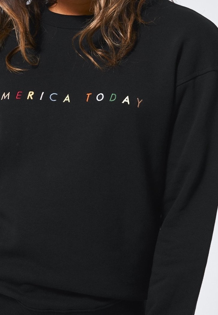 Mustapaita, jossa on pyöreä pääntie; rintamuksessa näkyy monivärinen "AMERICA TODAY" -kirjonta. Materiaali näyttää pehmeältä ja teksturoidulta.