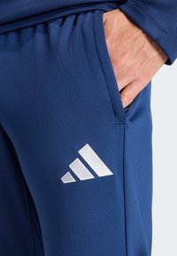 Σκούρες μπλε αθλητικές παντελόνες με λευκό κεντημένο λογότυπο τριών ρίγων, με λεία υφή, πλαϊνή τσέπη και σχεδιασμό με εφαρμοστή μέση.