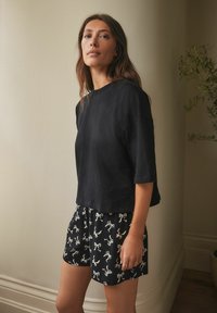 Black short-sleeve cotton top paired with patterned black shorts featuring light-colored illustrations of figures. Simple, relaxed fit design.