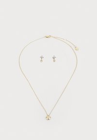 Goldene Halskette mit einem Herz-Anhänger und einer Kette, begleitet von silbernen Ohrsteckern mit einem kleinen dekorativen Design.