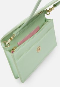 Liten mintgrön läderhandväska med guldsnäpp, rosa innerficka, dragkedjeavdelning och avtagbara axelbandsklipp.