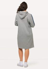 Abito lungo grigio con cappuccio, dotato di strisce laterali blu e taglio dritto, abbinato a sneakers bianche alte.