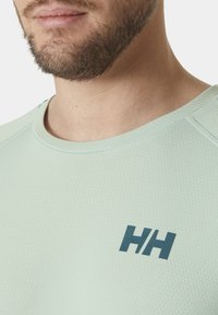 Lichtgroen sportshirt van textuurstof, met een ronde halslijn en een contrasterend donkerblauw logo op de borst.