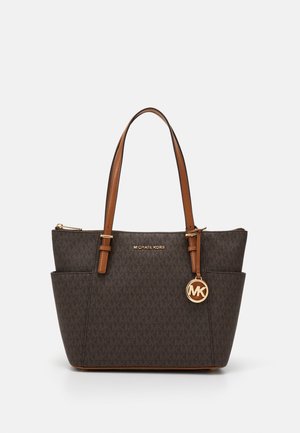 Brązowa torba typu tote marki Michael Kors z monogramem, jasnobrązowymi uchwytami, bocznymi kieszeniami, złotym breloczkiem z logo oraz zamkiem błyskawicznym na górze.
