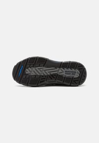 Semelle de chaussure en caoutchouc noir avec surface texturée, présentant un motif en chevrons et un branding "GoodYear". Design de grip renforcé pour une meilleure traction.