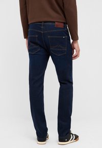 Granatowe dżinsy o prostym kroju z brązową skórzaną naszywką, dwoma tylnymi kieszeniami z falistym wzorem i kontrastującym przeszyciem.