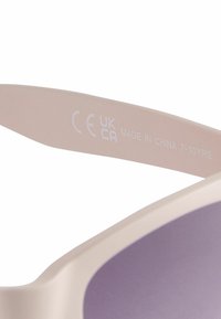 Lunettes de soleil pour enfants en rose clair avec une lentille violette et une monture en plastique lisse. Le côté intérieur de la branche présente des marquages de certification.