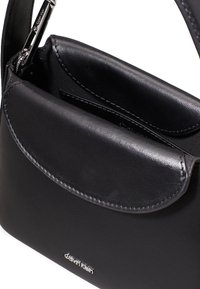 Borsa a tracolla in pelle nera con una superficie liscia, chiusura a patta e hardware in argento. Presenta un compartimento interno con due tasche.