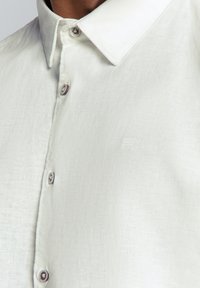 Lichtgekleurde linnen overhemd met een button-down kraag, voorzien van een subtiele structuur en grijze knopen met ronde details langs de sluiting.