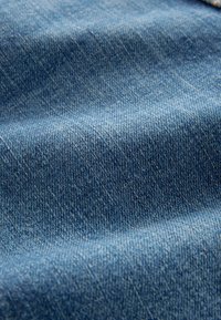 Gros plan d'un tissu en denim bleu montrant la texture détaillée du tissage et des plis subtils.