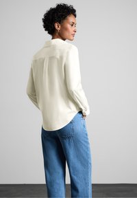 Cremefarvet skjorte med lange ærmer og krave, glat tekstur og lige snit. Parret med løstsiddende blå denim jeans. Afslappet look.