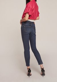 Röd kort topp med volangärmar kombinerad med mörkblå tajta jeans. Höga klackar fulländar outfiten. Jeans har en klassisk femfickdesign.