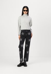 Šedý rebrovaný rolák, čierne džínsy so striebornými hviezdami, čierne platformové topánky, nosené modelkou s dlhými čiernymi vlasmi.