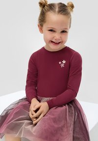 Robe maroon à manches longues avec une jupe en tulle superposée dans des nuances de rose et de violet. Présente une broderie florale sur la poitrine. Tissu doux et texturé.