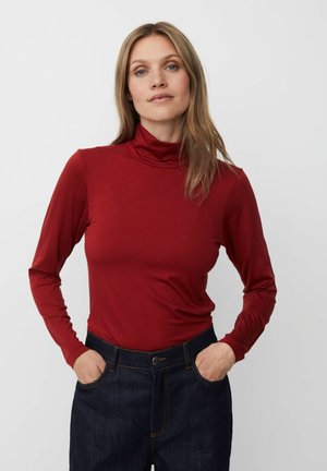 Rode langetermijn turtleneck top van zachte, gladde stof; gecombineerd met donkere spijkerbroeken met voorzakken en zichtbare stiksels.