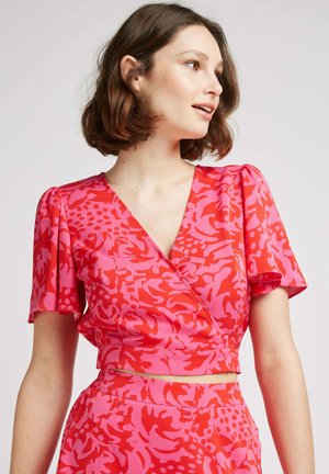 Haut enveloppant rose avec des manches bouffantes courtes, arborant un motif floral audacieux dans des nuances variées de rose et de rouge, coupé à la taille.