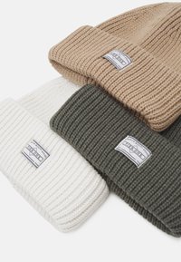 Tre strikkede beanie-hatte i beige, hvid og mørkegrøn. Hver hat har en ribbet struktur og et mærketapet på fronten.
