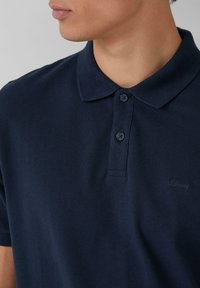 Tumesinise polo särk tekstuuriga kangast, kahe nööbiga esiosa ja peene logo tikandiga rinnal. Klassikaline krae disain.