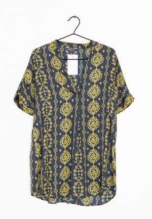 Blouse à manches courtes en tissu bleu foncé avec des motifs floraux et géométriques jaunes, à coupe ample et avec un col à boutons.