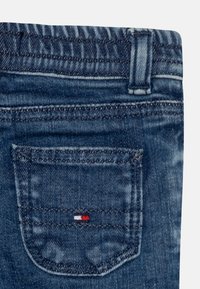 Ciemnoniebieskie dżinsy z tylnej kieszeni z małym logo w kolorach czerwonym, białym i niebieskim. Tkanina ma gładką fakturę z subtelnym wyblaknięciem.