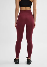 Bordeauxfarbene, hochtaillierte Leggings mit glatter Textur und figurbetontem Design, die ein dezentes Zickzackmuster am Bund und an den Knöchelbündchen aufweisen.
