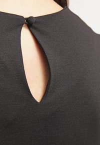 Black textile top featuring a keyhole back design, secured with a small button. The fabric has a smooth, slightly textured finish.