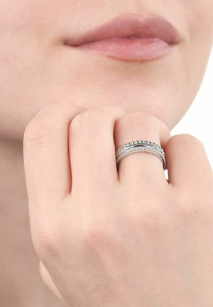 Nahaufnahme einer Hand in der Nähe der Lippen, die zwei silberne Ringe mit kleinen, filigranen Perlen- und Kristalldetails am Mittelfinger trägt.