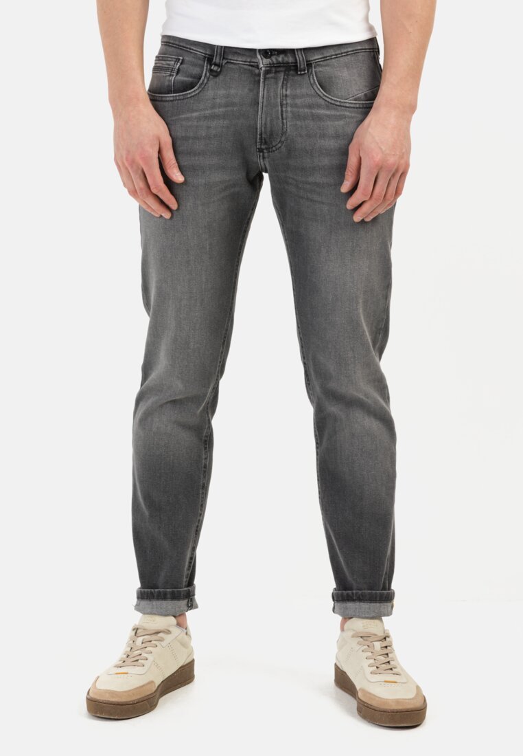 Jean en denim gris avec une coupe slim, cinq poches et des ourlets roulés, associés à des baskets beiges avec un design texturé et des accents clairs.