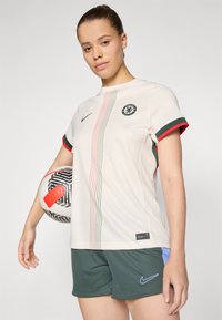 Nike jalkapallopaita vaaleassa kermanvärisessä sävyssä, jossa tummanvihreitä ja punaisia yksityiskohtia; paita sisältää pystysuoria viivoja ja seuran logon. Yhdistetty tummanvihreisiin shortseihin.
