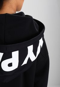 Black hooded sweatshirt featuring white branding on the back. Soft fabric with a relaxed fit and a large, adjustable hood.