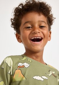 Maglietta verde a maniche corte con grafiche di dinosauro e vulcano. Il tessuto è morbido, con una vestibilità comoda e una scollatura rotonda con motivi a contrasto.