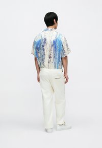 Koszula z krótkim rękawem w kolorze niebieskim i kremowym z teksturowanym wzorem rozprysków farby; zestawiona z kremowymi spodniami dresowymi z logo na tylnej kieszeni.