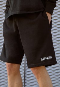 Shorts de jogging noirs en tissu doux, avec des poches latérales et un logo sur l'ourlet gauche. Design décontracté avec une coupe ample et une longueur mi-cuisse.
