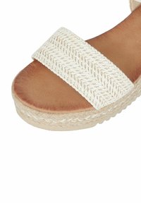 Sandalo bianco con cinturino intrecciato, fondo in pelle marrone e suola avvolta in juta. Superficie texture con suola piatta e dettagli di cucitura sottili.