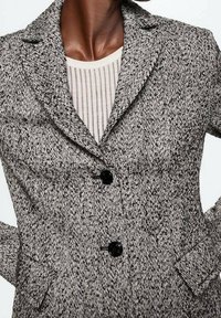 Zwart-witte getextureerde blazer met een reverskraag, twee zwarte knopen en zijzakken. Gemaakt van een geweven stof met een subtiel patroon.