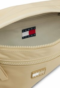 Interno di una borsa in nylon beige, con chiusura a zip, fodera testurizzata e un'etichetta con accenti rossi, bianchi e blu. Si nota un piccolo logo del marchio.