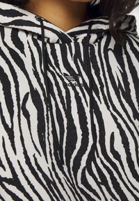 Sudadera con rayas de cebra en blanco y negro, con cordón y logo de Adidas. Fabricada en tela suave con un acabado texturizado.