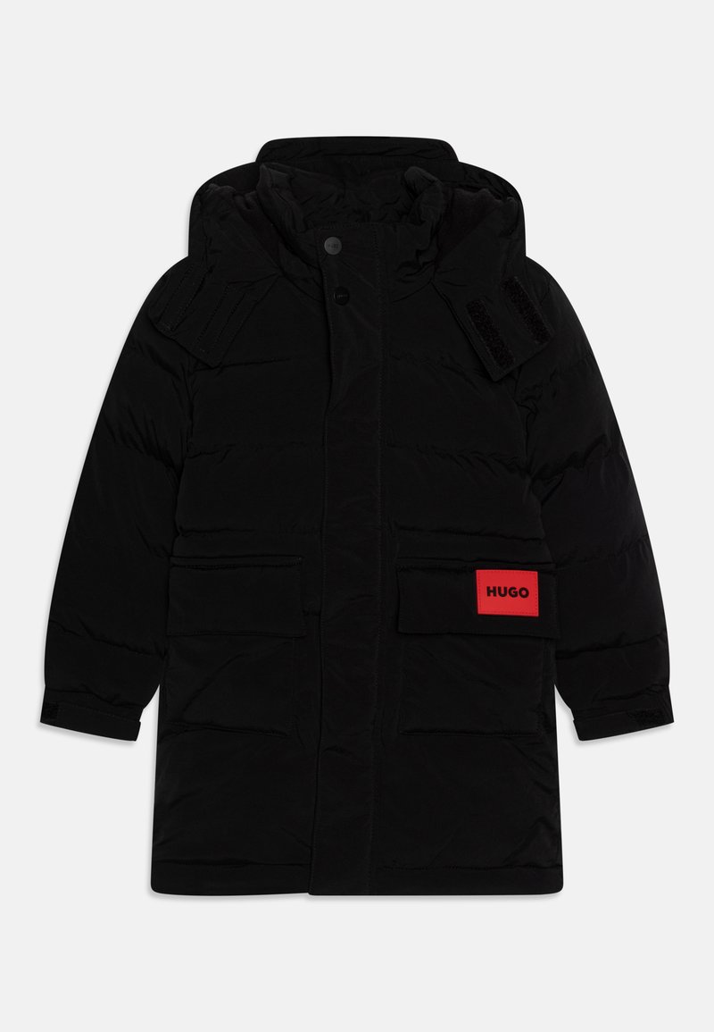 Svart polstret vinterjakke med hette, som har to frontlommer, teksturerte skulderdetaljer og en fremtredende rød «Hugo»-etikett.
